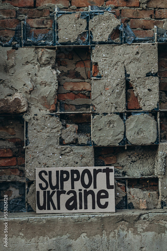 Ukrainian protest against war with banner  placard  with inscription message text Support Ukraine  ruined city background. Crisis  peace  Russian aggression invasion concept. anti-war demonstration.