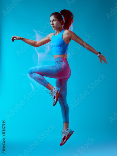 Fototapeta Naklejka Na Ścianę i Meble -  A fit sportswoman jumping and doing exercises. Long exposure capture movement.