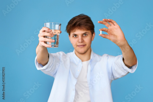 man holding pill and glass of water on blue background