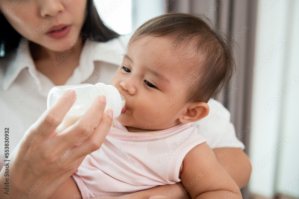A baby girl is drinking milk bottle in mother arms, family, child, childhood and parenthood concept A baby girl is drinking milk bottle in mother arms, family, child, childhood and parenthood concept