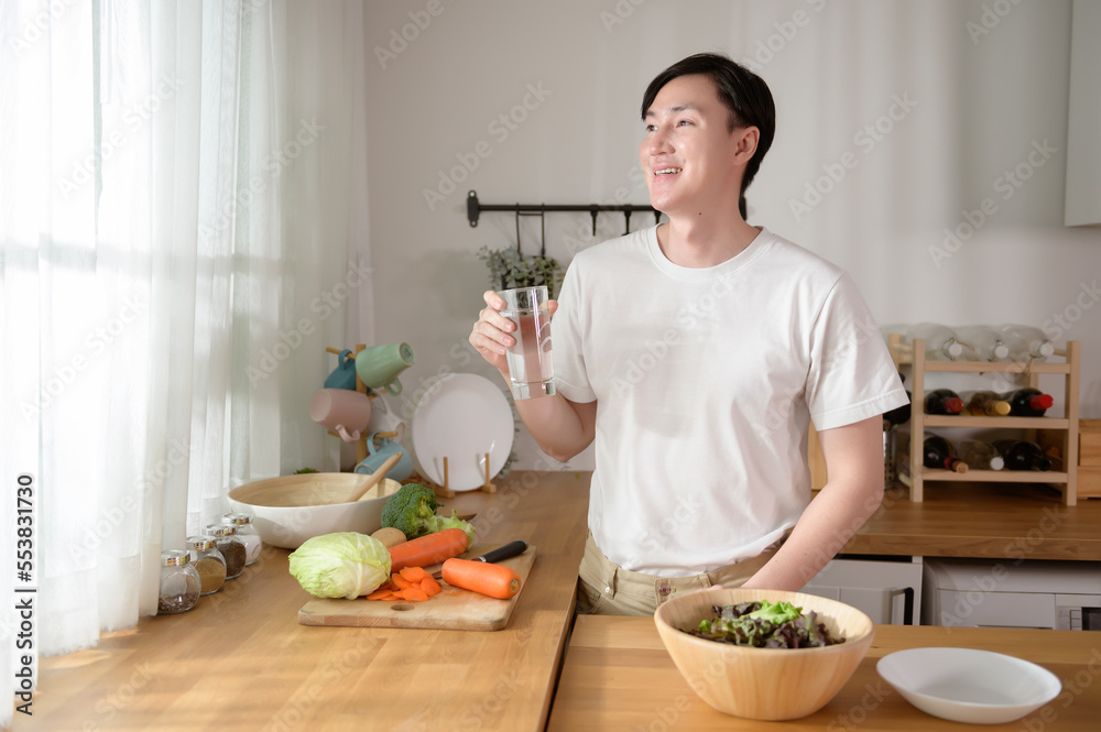 An Asian young man drinking fresh water in kitchen at home , healthy lifestyle concept An Asian young man drinking fresh water in kitchen at home , healthy lifestyle concept
