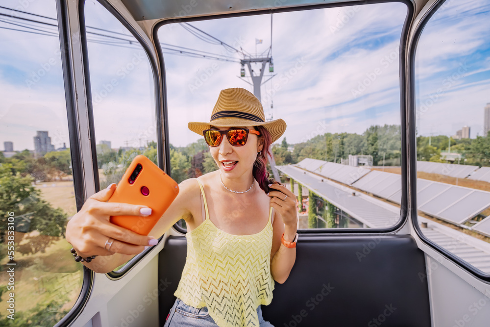 Naklejka premium A travel blogger girl takes a selfie photo on a smartphone in a cable car with a view of the city of Cologne