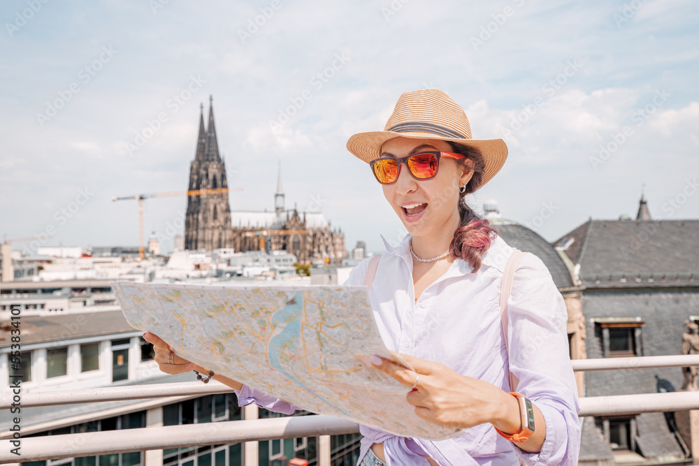 Tourist girl with maps, navigating for sights and landmarks and geolocating on the streets of an old European city. Cologne cathedral in the background