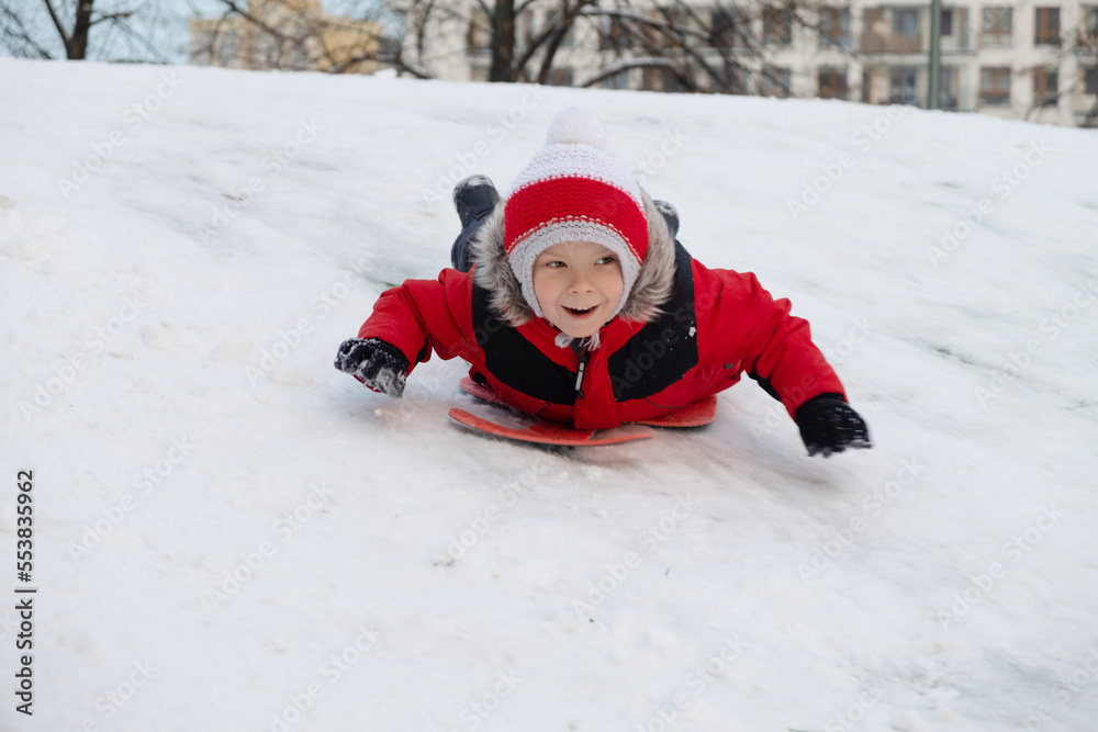 The boy climbs down on a sledge on a hill