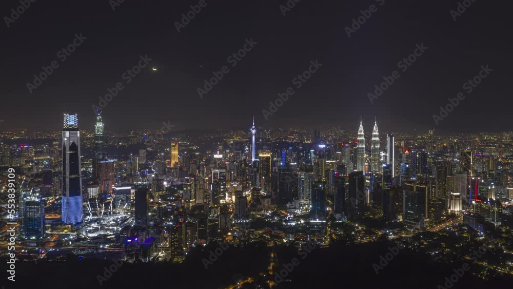 Aerial high angle night view time lapse overlooking busy city streets and a moon setting against a city skyline in Kuala Lumpur, Malaysia. Prores 4KUHD Timelapse. Aerial high angle night view time lapse overlooking busy city streets and a moon setting against a city skyline in Kuala Lumpur, Malaysia. Prores 4KUHD Timelapse.