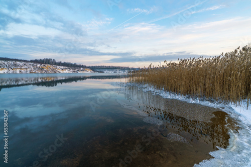 A mirror image of the sky and the shore with a snow cover on the reservoir .