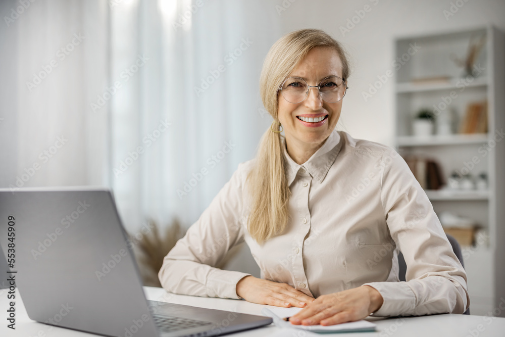 Portrait of beautiful middle-aged businesslady sitting at her workplace in the office and smiling to camera, successful woman Portrait of beautiful middle-aged businesslady sitting at her workplace in the office and smiling to camera, successful woman