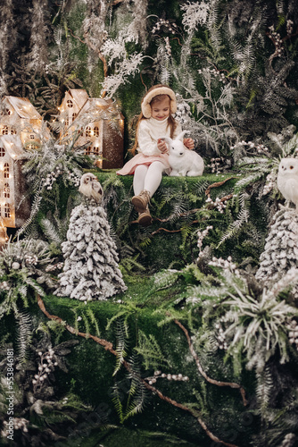 picture of beauatiful little girl in sits in a christmas decoration with trees and a little white rabbit photo