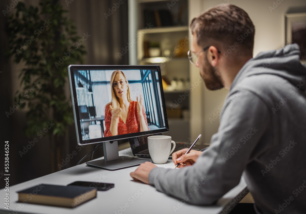 Young businessman having videochat with colleague and making notes of ideas, brainstorming