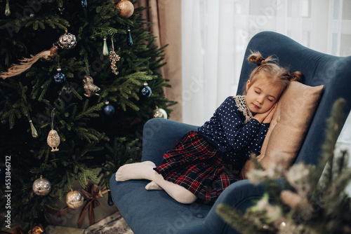 picutre of pretty girl sleeps near the christmas tree on a blue armchair in the living-room photo