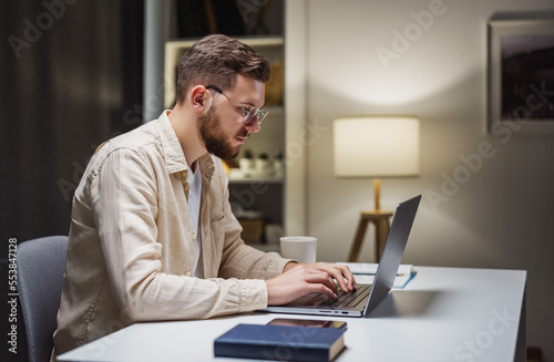 Young caucasian businessman in eyglasses working on computer at home, remote employment