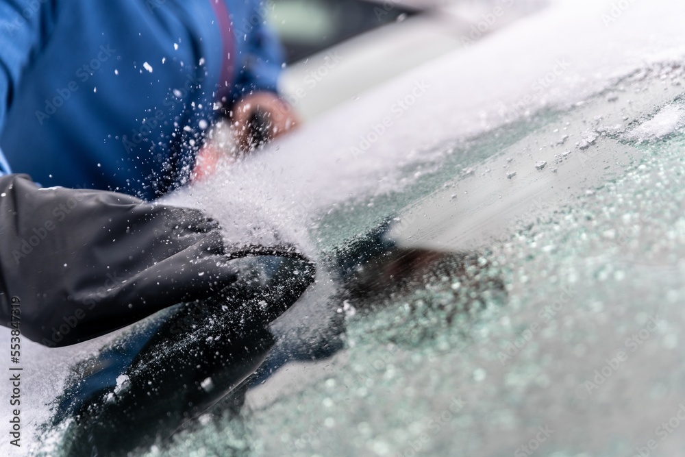 Fototapeta premium man uses ice scrapers to thaw an ice-covered car windshield