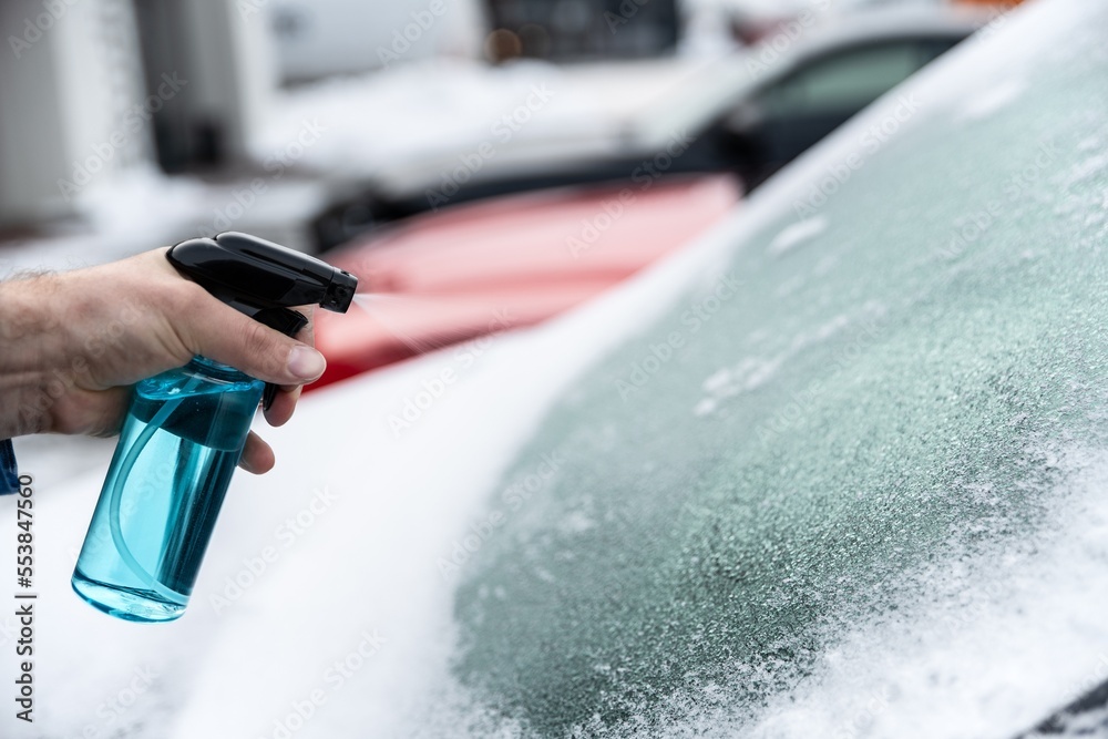 Man uses a bottle of de-icer to defrost the ice-covered windshield