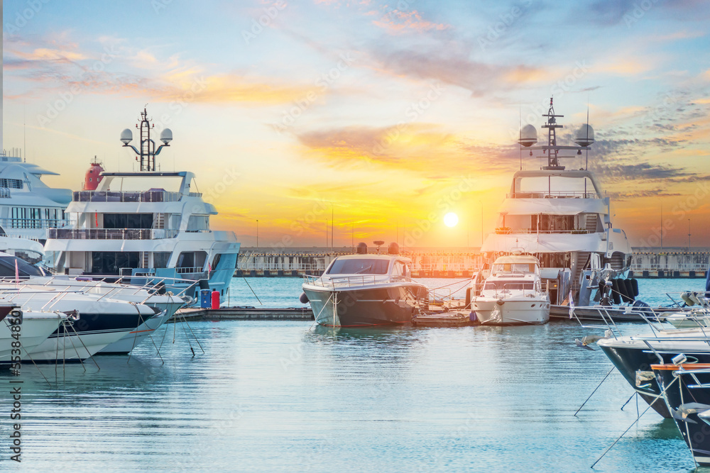 Naklejka premium Marine parking of modern motor boats and blue water. Luxury yachts docked in sea port at sunset. Tranquility, relaxation and fashionable vacation.