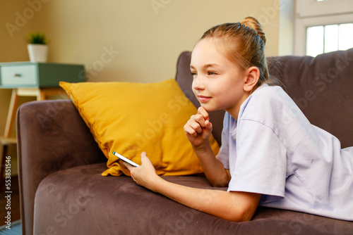 cute little girl useing smartphone and lying down on sofa in viving room at her home photo