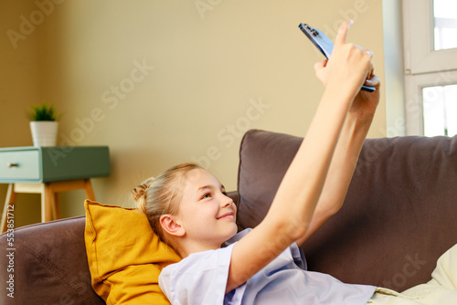 cute little girl useing smartphone and lying down on sofa in viving room at her home photo