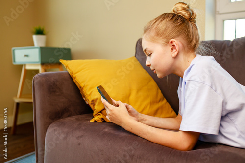 cute little girl useing smartphone and lying down on sofa in viving room at her home photo