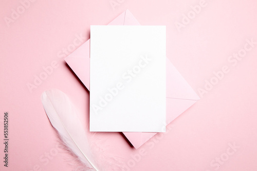 Holiday greeting card mockup with pink envelope and white feather on light pink background, top view, flat lay. Blank wedding invitation or Valentine Day letter, empty card © mikeosphoto