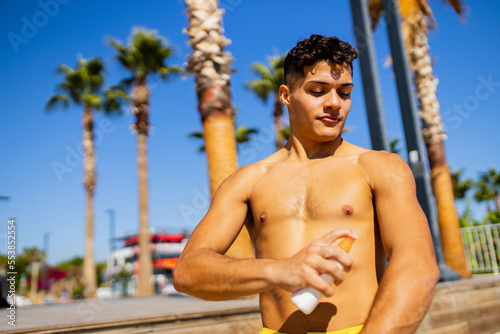 latin man applying suntan lotion at sea with palms background