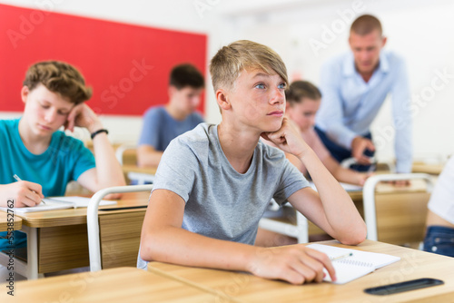 Portrait of surprised teenage boy sitting at table in classroom during lesson