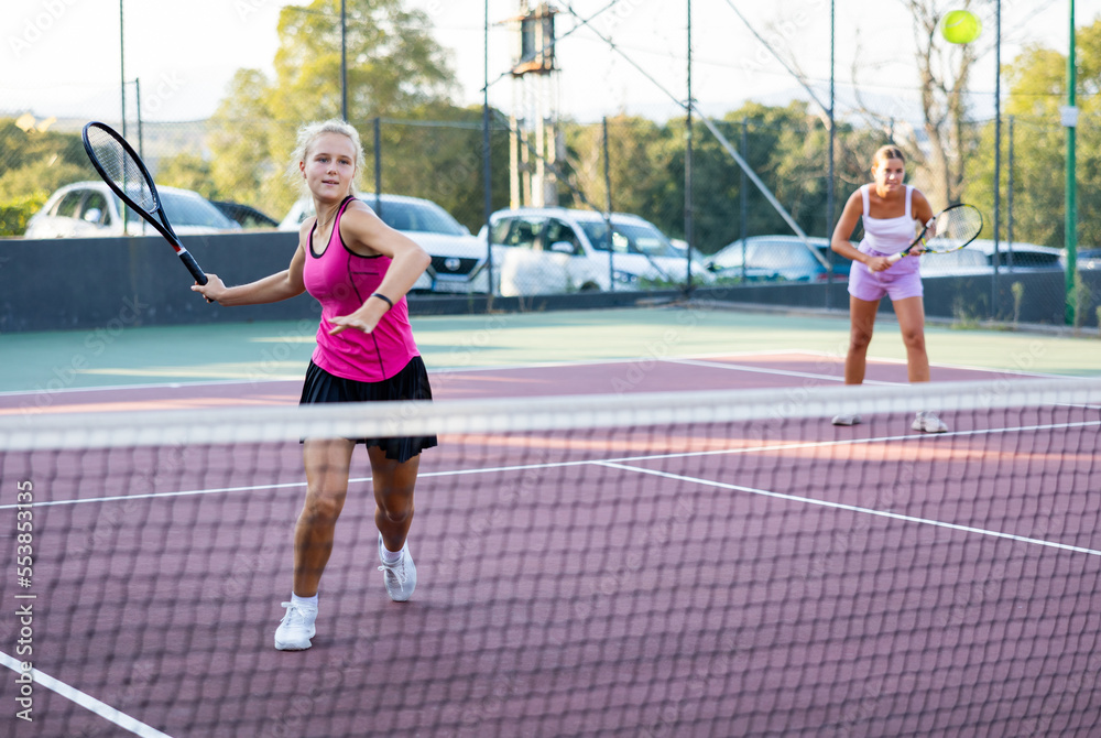 Sportive woman dressed in t-shirt and skirt playing tennis together with partner