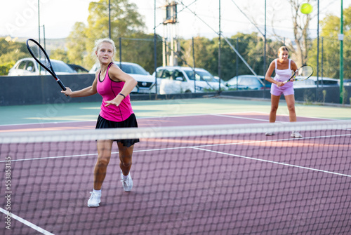 Sportive woman dressed in t-shirt and skirt playing tennis together with partner