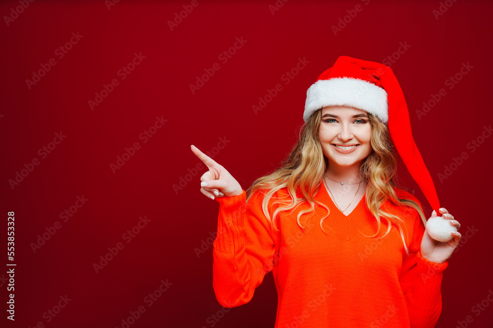 banner. a beautiful woman in a Santa Claus hat points finger to red background. banner. a beautiful woman in a Santa Claus hat points finger to red background.