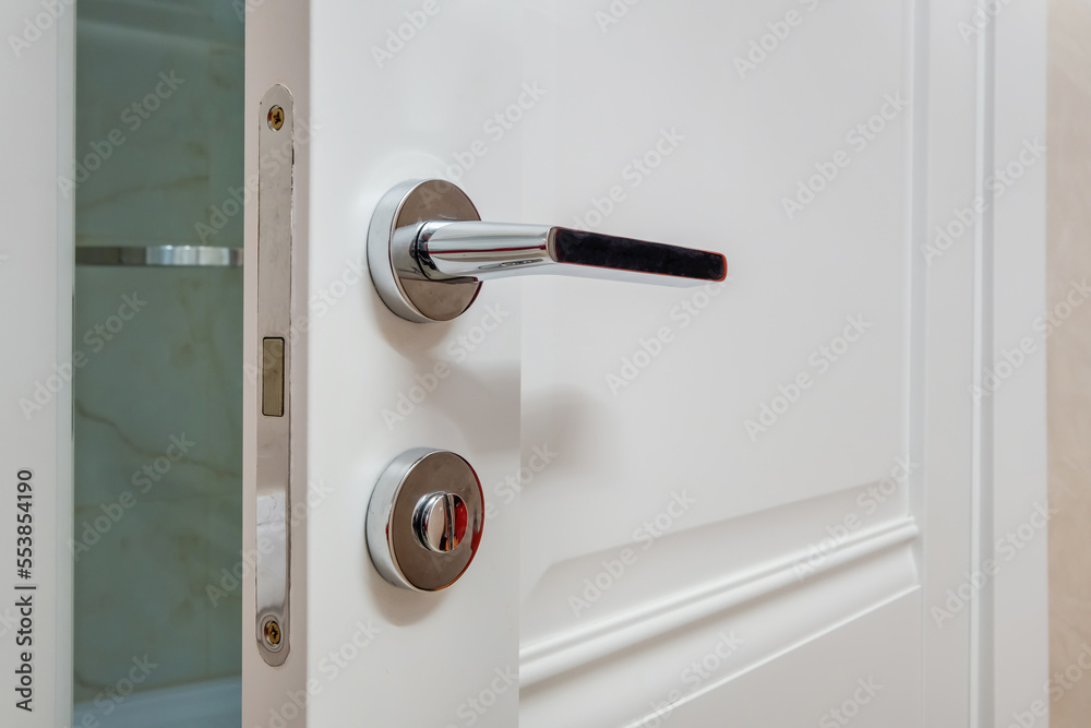 Modern metal door handle on white wooden door in interior. Knob close-up elements. Door handle, fittings for interior design Modern metal door handle on white wooden door in interior. Knob close-up elements. Door handle, fittings for interior design