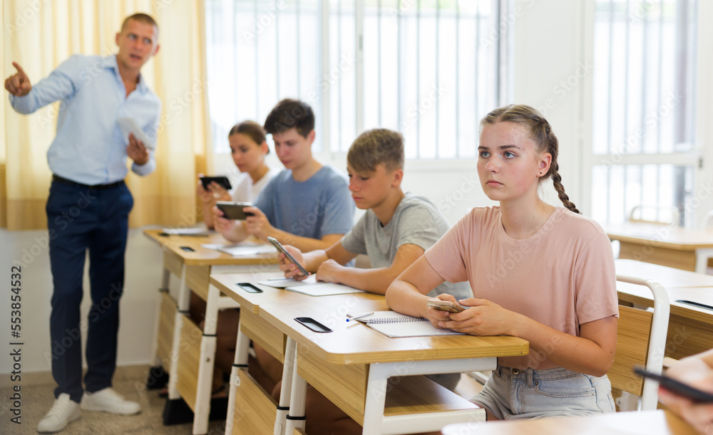 Interested teen girl student using smartphone while studying in college with group of classmates..