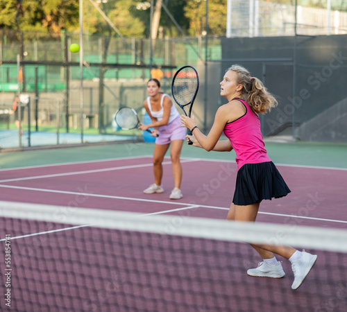 Young woman and her female partner playing tennis on court during friendly match outdoor