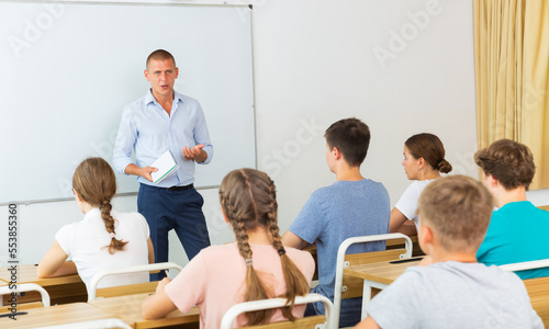 Teacher explaining studying material to teenagers during lesson at school  standing at whiteboard..