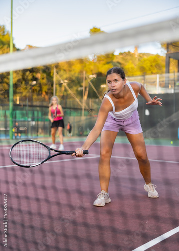 Sporty teenage girl tennis player playing tennis at court outdoor. View through tennis net