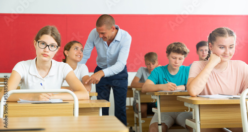 Teenage students are sitting at their desks in classroom. In background the teacher. High quality photo