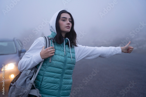 Slika na platnu Woman hitch-hiking for a car at the foggy mountains
