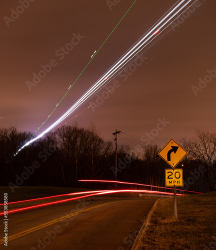 Airplane light trails over road with car light trails and speed limit sign long exposure shot.