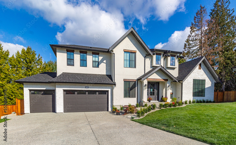 Wide angle shot of front view of luxury two garage big white home with luscious green grass  on a blue sky day in the suburbs.