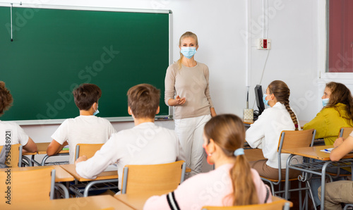 Female speaker in protective mask giving lesson for teenage students in classroom