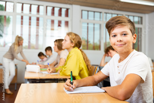 Portrait of positive schoolboy posing in classroom during lesson in secondary school photo