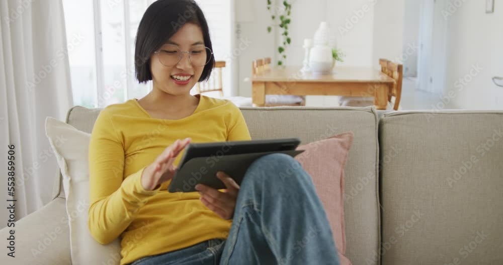 Happy asian woman using tablet and sitting on couch in living room Happy asian woman using tablet and sitting on couch in living room
