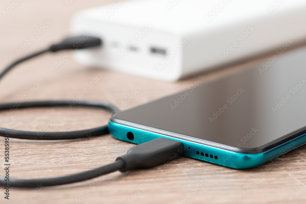 Charging the battery of smartphone, powerbank on the background, close up. Staying connected with digital world, modern devices concept
