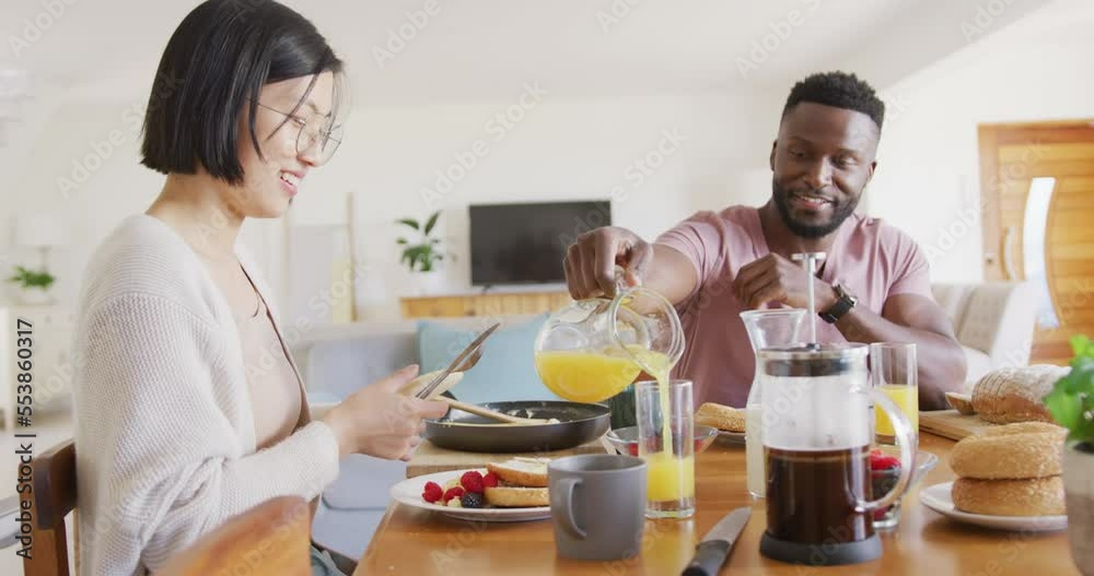 Happy diverse couple sitting at table and having breakfast Happy diverse couple sitting at table and having breakfast