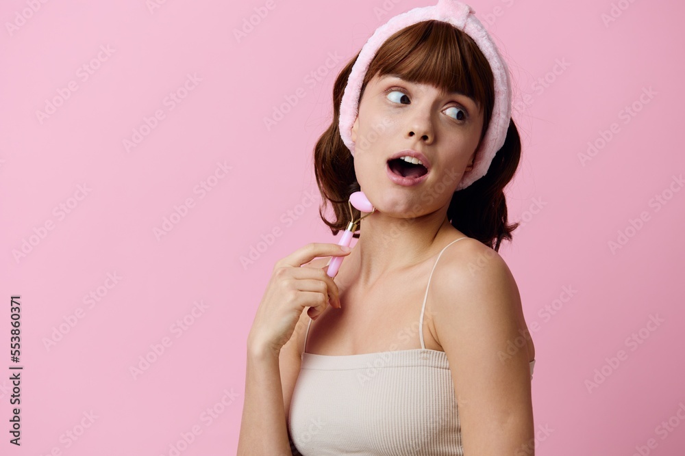 a close-up photo of a happy, delighted woman emotionally posing standing on a pink background and holding a roller facial massager