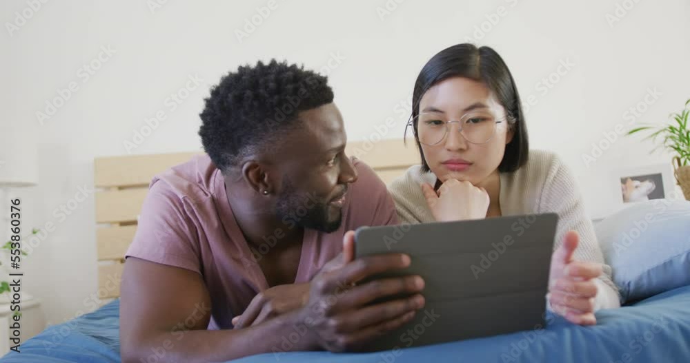 Happy diverse couple using tablet and lying in bedroom Happy diverse couple using tablet and lying in bedroom