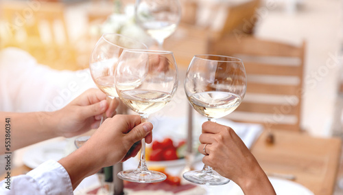 Dinner wood table hand of friends clinking glasses of white wine with sunlight, closeup © Parilov