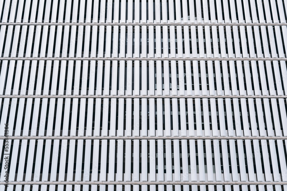Ultra-modern facade of a building in a sequential pattern of rectangular white plates made of metal that preserve privacy inside the building and allow it to receive sunlight inside Ultra-modern facade of a building in a sequential pattern of rectangular white plates made of metal that preserve privacy inside the building and allow it to receive sunlight inside