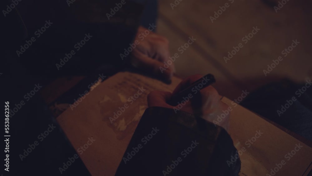 Adult seriously man with beard write old diary wear a vintage leather jacket in retro small fishing house of wood at deep night. Vintage a kerosene lamp fire