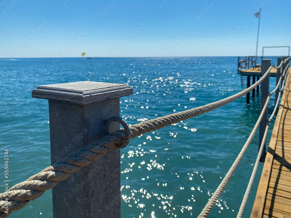 Fototapeta premium A wooden long pontoon, a pier with a rope railing on the sea on the beach on vacation in a paradise warm eastern tropical country resort