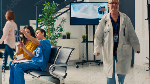 Medical assistant explaining radiography scan to asian patient, looking at bones x ray results to talk about healthcare diagnosis. Analyzing orthopedic disease in waiting area. Tripod shot. photo