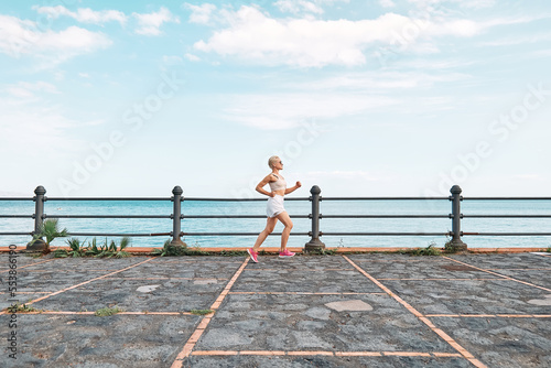 Young attractive sportive woman running on seaside promenade. Workout outdoors by the sea. Fitness, sport and healthy lifestyle concept.