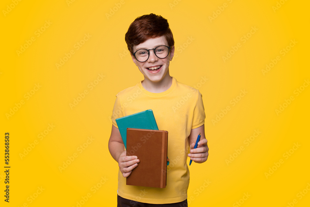 Little smiling boy, holding books and pencil in front of him. Back to school concepts on yellow background with. School education. Learning concept. Looking Little smiling boy, holding books and pencil in front of him. Back to school concepts on yellow background with. School education. Learning concept. Looking